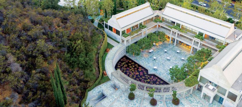 Aerial photo of the Skirball campus focusing on a courtyard with a lily pond surrounded by 3 main building and a large hill.
