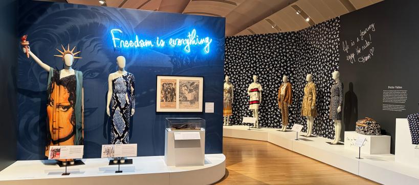 A wide gallery photo showing mannequins in dresses and a neon sign in blue that says Freedom is Everything.