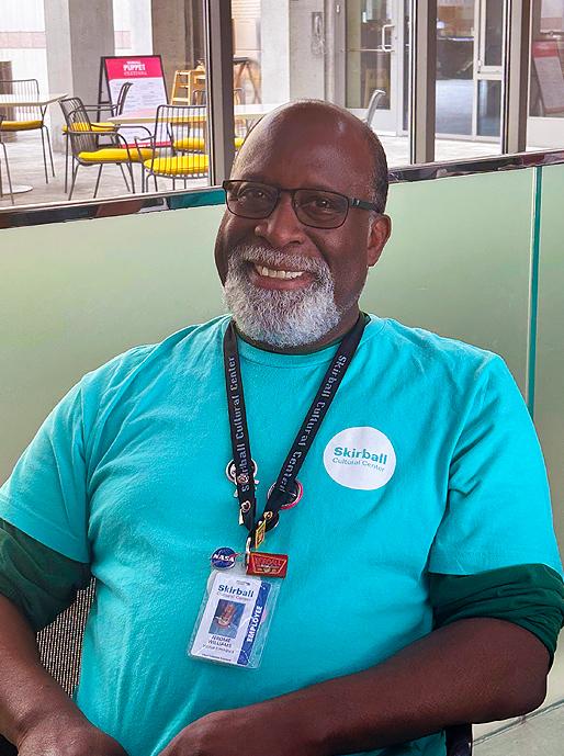 A male employee smiles from behind a visitor services desk.