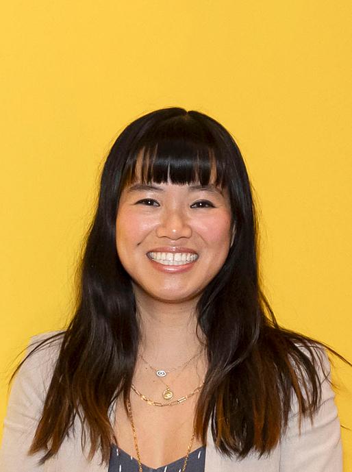 A headshot of Vicky smiling in front of a bright yellow wall.