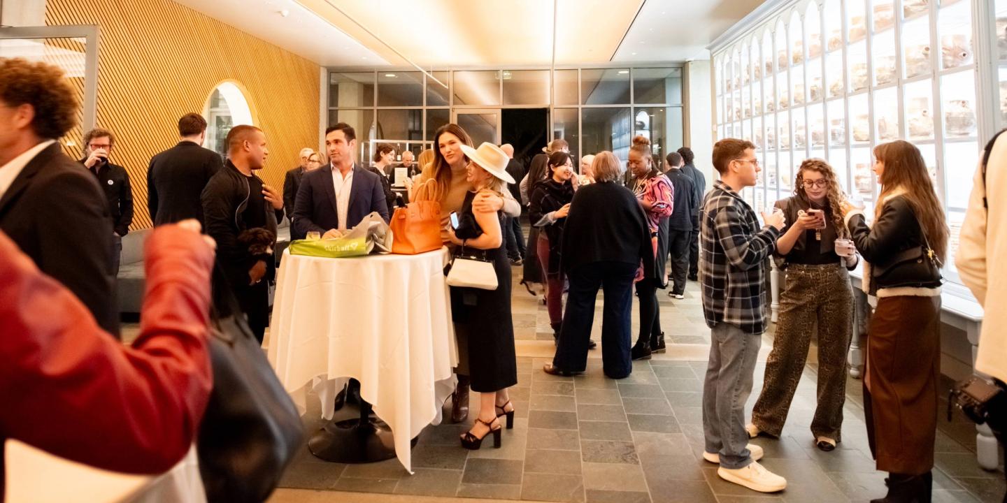 People gather in Ruby Commons at the Skirball talking amongst themselves with refreshments.