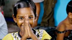 a young girl holding her hands up in front of her face in an expression of thanks