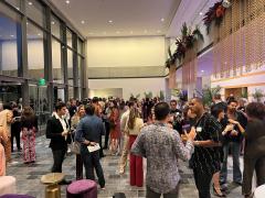 A group of people gathering in a long hall dressed in business attire conversing.