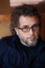 close up image of a man with curly hair, glasses, beard, and a black shirt
