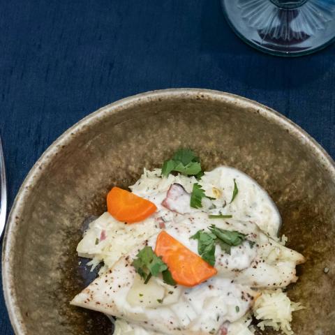 A table set for a meal with ceramic plate and cup on a blue cloth. The plate holds cooked fish and vegetables.