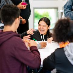 A teen smiling at a table while working with other teens.