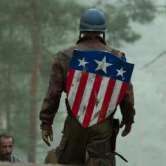 Still from the film showing Captain America walking towards a group of soldiers in a field wearing the iconic Stars and Stripes shield on his back.