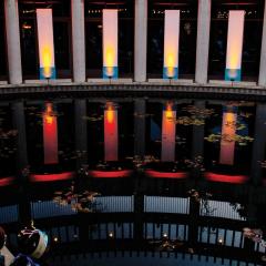 Photo of the lily pond at the Skirball lit up with large column spotlights mimicking a Hanukkah. Families stand along the pond looking at the lights.